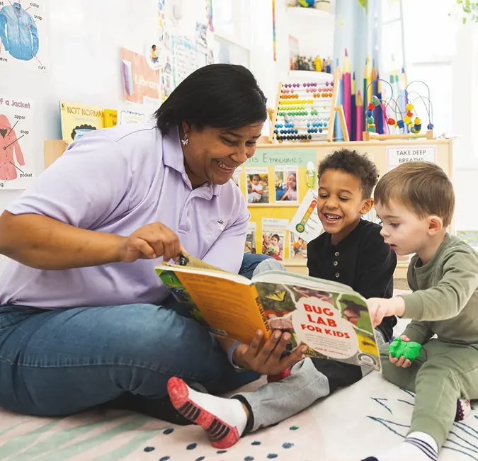 Adult sharing a book with young children seated on the floor.